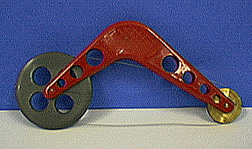 A red metal toy with a gray wheel and a gold-colored wheel. A dark wire extends from the large wheel to the smaller wheel.