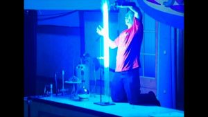 Demonstrator holding a torch over a lit tube filled with bright flames and white illumination.