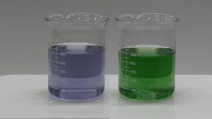 Two beakers with stir bars, one with clear purple liquid and a second with a clear green liquid