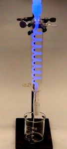 A photo shows blue liquid flowing through a tube into a beaker. In the second photo, a set up of a tube with blue liquid above a beaker