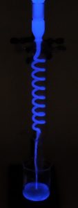 A photo shows blue liquid flowing through a tube into a beaker. In the second photo, a set up of a tube with blue liquid above a beaker